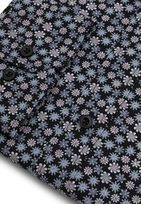 Czarna koszula z tkaniny z kwiatowym wzorem w odcieniach fioletu i niebieskiego. Dwa czarne guziki widoczne przy kołnierzyku, o gładkiej fakturze.