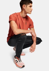 Sportstøj bestående af en koralfarvet T-shirt med korte ærmer, sorte tapered pants og lyserøde løbesko med hvide detaljer og sorte snørebånd.