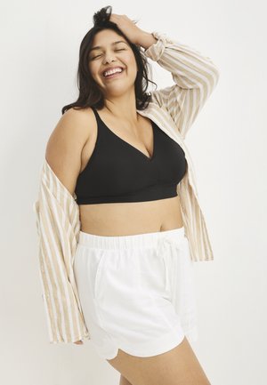 Black v-neck bralette paired with white shorts. The model is wearing a light striped button-up, with a soft texture and relaxed fit.