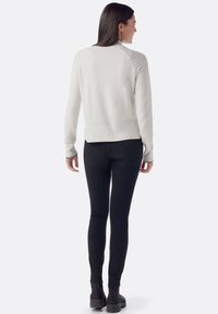 Maglione color crema con texture a coste e maniche lunghe, abbinato a jeans skinny neri e stivaletti, visto da dietro.