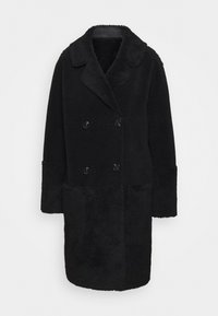 Svart fuskpälsjacka med dubbelknäppt fram, snedskuren krage och långa ärmar. Jackan har strukturerad tyg och svarta knappar.