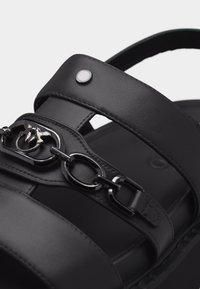 Μαύρο δερμάτινο σανδάλι με διπλά λουριά, που διαθέτει μαύρη μεταλλική αλυσίδα και λογότυπο στο μπροστινό λουρί με ένα μικρό ασημένιο καρφί.