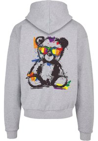 Felpa grigia con una grafica di un orsetto colorato sulla schiena, caratterizzato da occhiali da sole vivaci e spruzzi di colore. Tessuto in cotone, design casual.