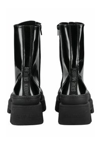 Botines de charol negro con suela de goma gruesa, cierre de cremallera lateral y marca en relieve en el talón trasero.