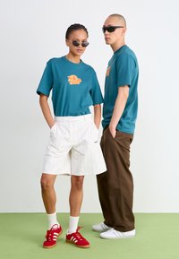Teal t-shirts with orange graphic, white pinstriped shorts, and red sneakers. Accessories include black sunglasses and white socks.