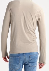 Beige Langarmhemd aus glattem Stoff, taillierte Passform, mit rundem Halsausschnitt und subtiler Dehnung, kombiniert mit blauen Jeans.