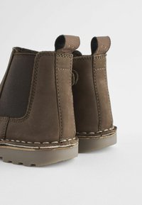 Stivaletti in suede marrone con pannelli laterali elastici, dettagli cuciti e linguette per la presa, dotati di una suola in gomma testurizzata.