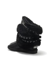 Black fur and leather boots with a curled design, featuring silver chain accents and a textured upper. Flat sole.