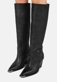 Bottes noires jusqu'aux genoux en matériau texturé avec un bout pointu et un talon compensé, équipées de fermetures éclair sur les côtés et de détails de couture décoratifs.