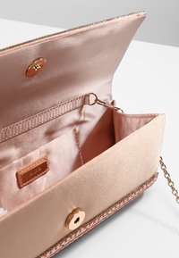 Jasnoróżowa satynowa kopertówka ze złotymi akcentami i łańcuszkiem, z pojemnym wnętrzem i kieszonką na zamek dla lepszej organizacji.