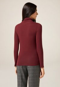 Bordowa bluzka z długim rękawem i golfem, wykonana z gładkiej tkaniny, dopasowanego kroju, z subtelnym, zawijanym kołnierzem i zwężanymi rękawami.