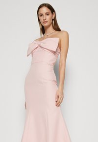Abito rosa senza spalline con un grande fiocco dettagliato sul collo, corpetto aderente e gonna svasata. Tessuto liscio e testurizzato. Design elegante.