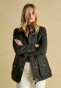 Giacca in lana verde scuro con un motivo a quadri, hardware dorato e due tasche frontali. Presenta una chiusura con zip e bottoni a pressione.