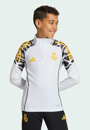 White athletic pullover with a quarter-zip, yellow accents, black and white patterned shoulders, and Real Madrid logo on the chest.