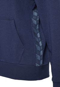 Dunkelblaues Hoodie mit Kängurutasche, strukturiertem Stoff und einem seitlichen Einsatz mit einem reflektierenden Logomuster. Weiches, lässiges Design.