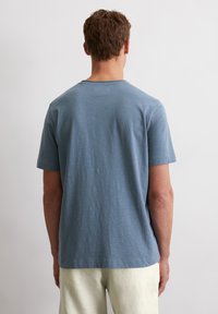 Herren T-Shirt mit kurzen Ärmeln aus weichem blauen Stoff, runder Ausschnitt, lockere Passform, mit einer subtilen Textur und ohne sichtbare Beschriftung auf der Rückseite.