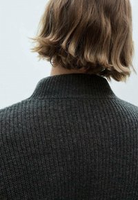Cheveux courts ondulés châtain clair sur une personne portant un pull gris foncé en tricot, vue de dos sur un fond uni.