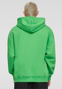 Sudadera verde con capucha forrada, corte oversize y puños acanalados. Confeccionada en material suave, con una textura lisa y costuras mínimas.