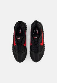 Zwarte sportschoenen met een gestructureerde bovenkant, rode accenten en zwarte veter. Heeft een prominente swoosh-logo en een dikke, gevormde zool.