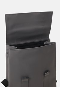 Sac à dos gris en matériau lisse et durable. Doté d'une fermeture à rabat, de bretelles réglables et d'un intérieur spacieux avec une doublure noire.