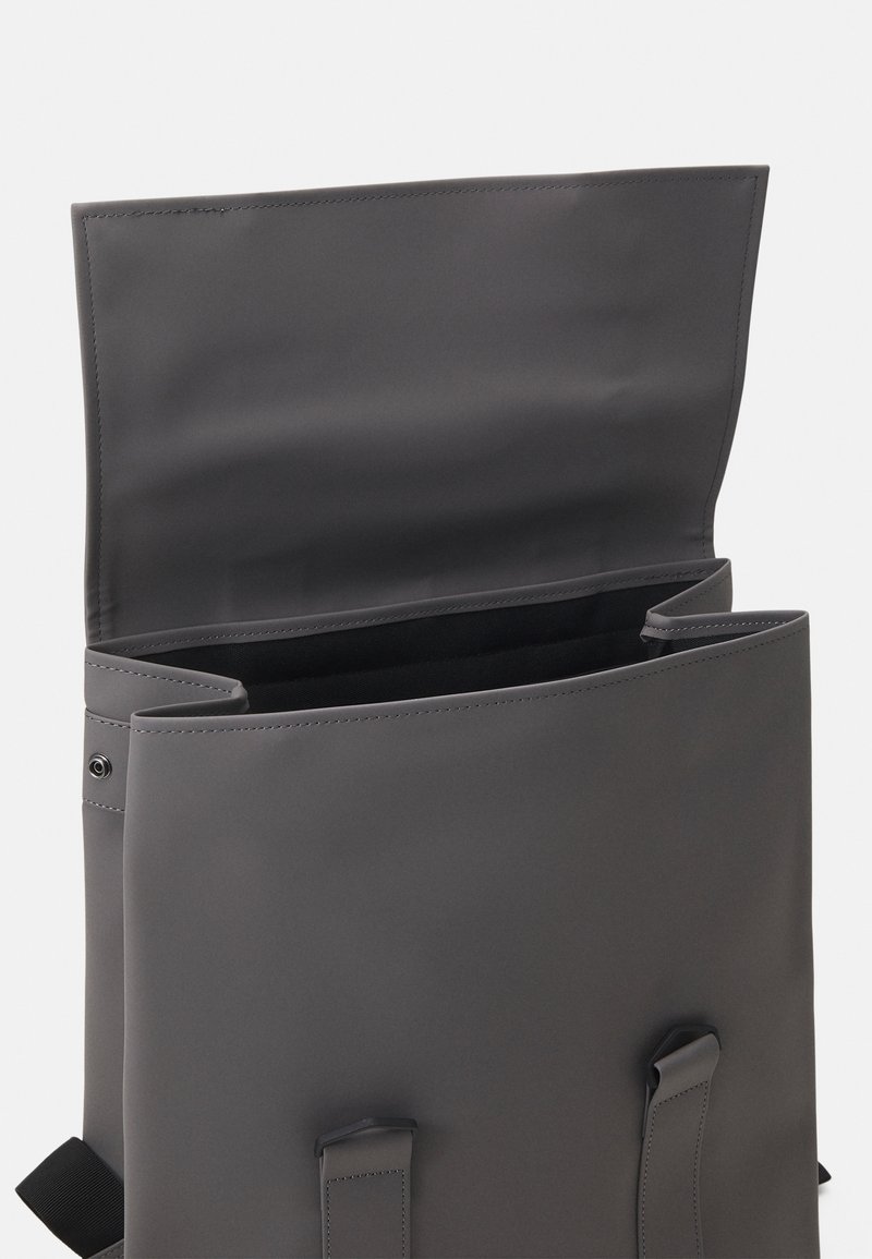 Zaino grigio realizzato in materiale liscio e resistente. Presenta una chiusura a patta, spallacci regolabili e un ampio interno foderato in nero.