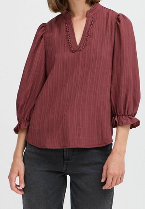 Bordeaux bluse med en struktureret finish, v-hals og flæseærmer. Har dekorativ syning langs halsudskæringen og en afslappet pasform.