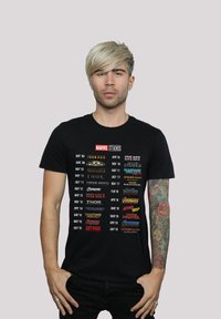 Black cotton t-shirt featuring a list of Marvel Studios movie titles and release dates in various colored fonts arranged vertically.