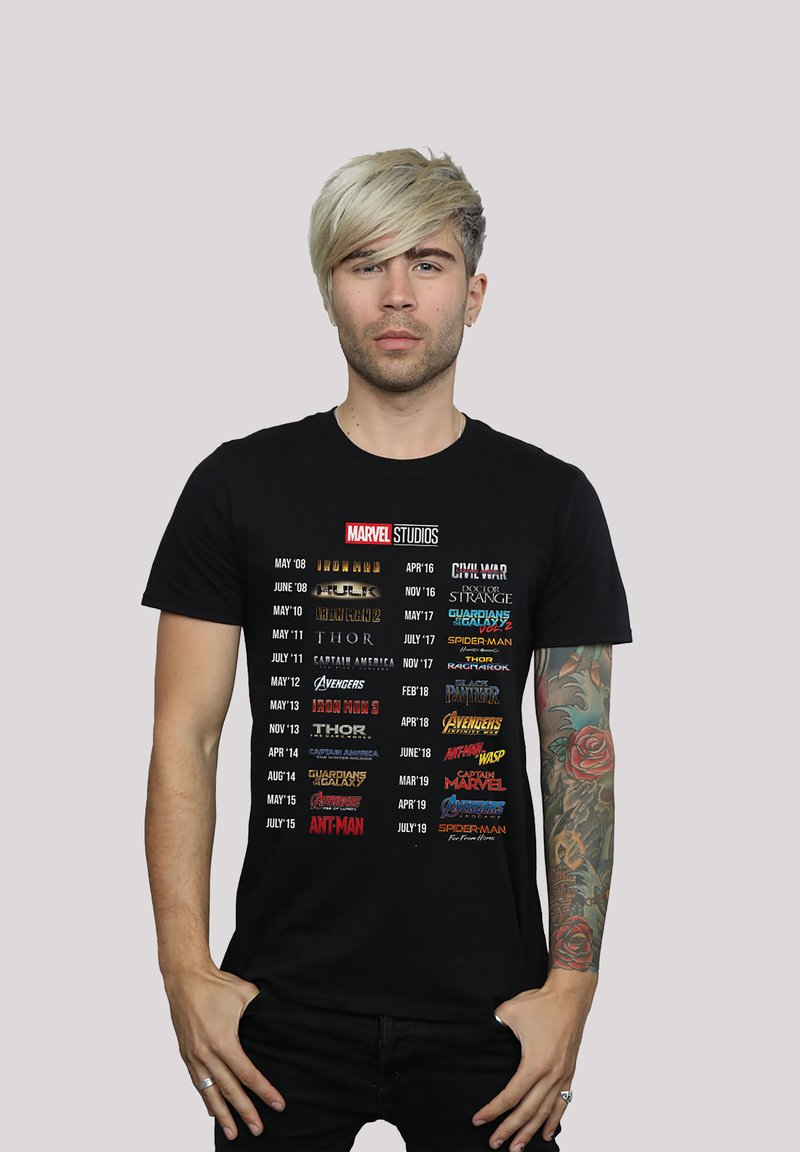 Black cotton t-shirt featuring a list of Marvel Studios movie titles and release dates in various colored fonts arranged vertically.