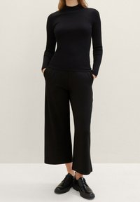 Maglietta nera a coste con maniche lunghe e collo alto, abbinata a pantaloni neri a gamba larga e scarpe nere con lacci; tessuto liscio e vestibilità su misura.
