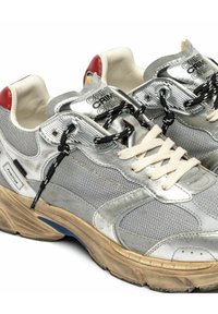 Baskets en mesh argenté et gris avec des lacets noirs et blancs, des languettes rouges à l'arrière, des semelles beiges, et la marque "CRIME LONDON" sur les côtés et les languettes.