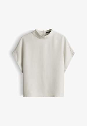 Beige blouse met korte mouwen, hoge halslijn en rits aan de achterkant, getoond tegen een witte achtergrond.