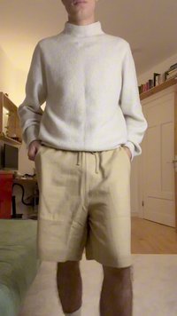 Crème coltrui met ribbelstructuur, gecombineerd met beige shorts. De trui heeft een hoge kraag; de shorts zijn losvallend en hebben een elastische tailleband.