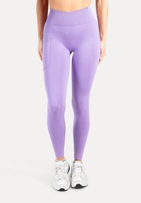 Paarse leggings met hoge taille, een gladde textuur en een zijzak; gecombineerd met witte sportschoenen.