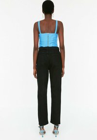 Top corto de mezclilla azul con cremallera en el centro, combinado con pantalones negros de cintura alta y sandalias de tacón azul claro.