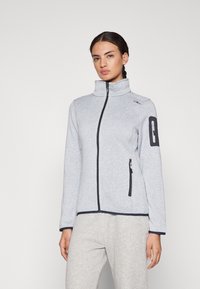 Veste zippée gris clair avec un col haut, fermeture éclair noire et accents. Dispose d'une poche zippée sur le bras gauche. Texture lisse.