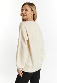 Krämfärgad stickad tröja med mjuk, texturerad yta, vida ärmar och ribbat fåll. Lätt oversize-design som visar upp en avslappnad passform.