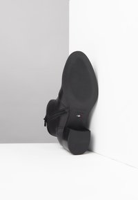 Schwarze Leder-Stiefelette mit runder Zehenpartie, seitlichem Reißverschluss und strukturiertem Sohle. Sie hat einen niedrigen Blockabsatz und eine Markenkennung auf der Sohle.