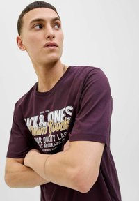 Bordo pamučna majica s okruglim izrezom i kratkim rukavima. Sadrži odvažne tiskane natpise u bijeloj i zlatnoj boji, naglašavajući detalje brenda i kvalitete.