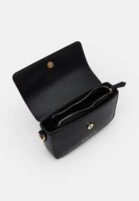 Bolsa de mão preta em pele com fecho de pressão dourado, apresentando um bolso interior com zíper e textura suave. O nome da marca está gravado na parte da frente.