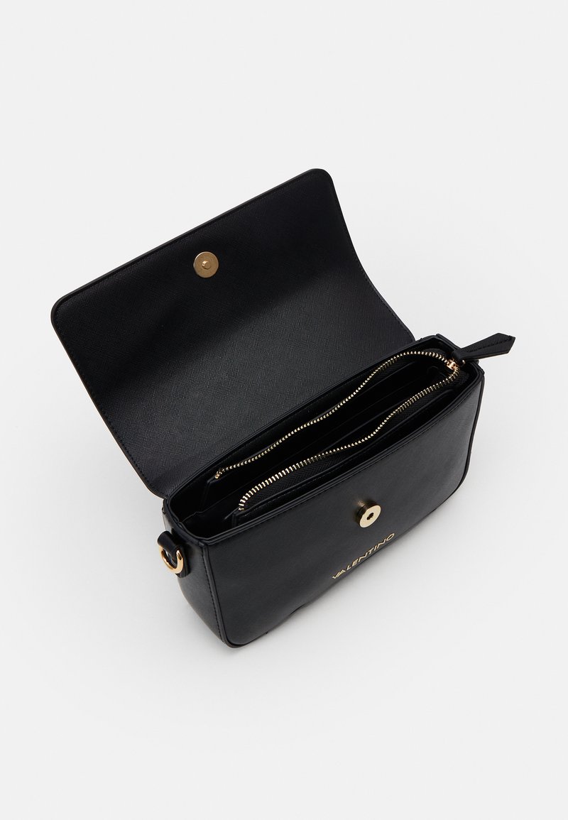 Sac à main en cuir noir avec une fermeture à pression dorée, doté d'une poche intérieure zippée et d'une texture lisse. Le nom de la marque est embossé sur le devant.