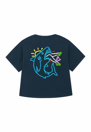 Marineblauw shirt met korte mouwen en een neonstijl grafiek van een haai die benen bijt met hoge hakken, met een gele zon op de achtergrond.