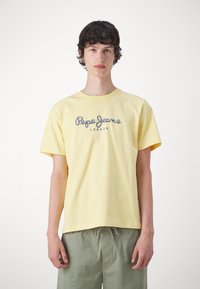 Geltona medvilninė marškinėlių su apvalia iškirpte ir trumpomis rankovėmis, kuriuose per krūtinę pavaizduotas tamsiai mėlynas "Pepe Jeans London" logotipas.