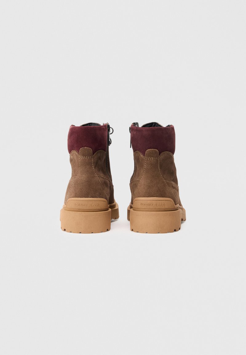 Brown suede ankle boots with a burgundy upper, zip closure, and rubber soles. Features a textured surface and visible logo on the heel.