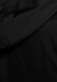 Czarna tkanina o gładkiej fakturze, z detale szwu i subtelnym połyskiem. Tkanina wydaje się lekka i elastyczna.