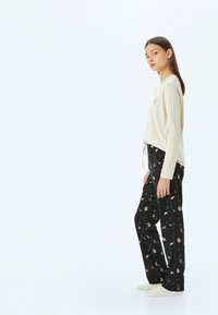 Lichtbeige lange mouw top met strikdetail, gecombineerd met zwarte broek met een patroon van verschillende kleine illustraties. Zachte textuur, casual pasvorm.