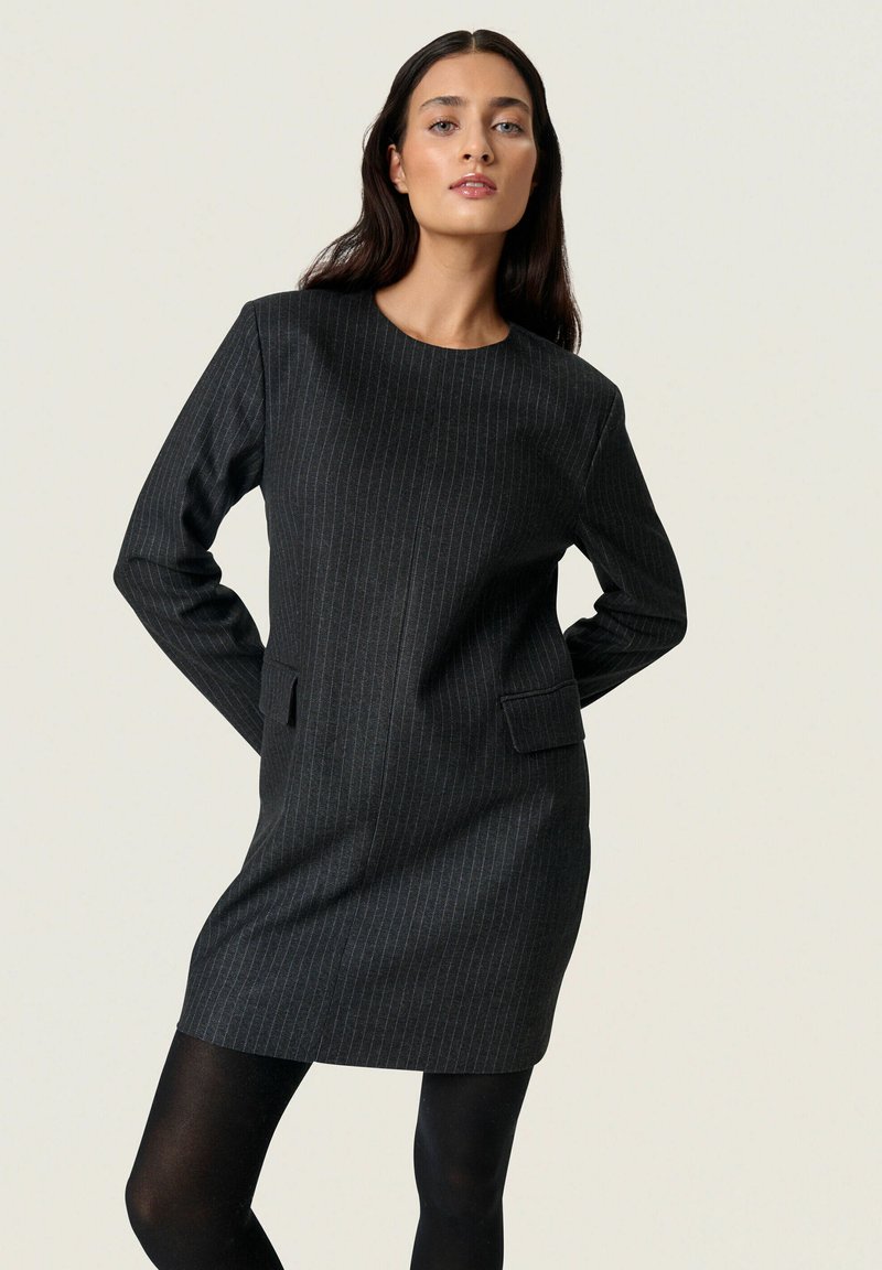 Kátrány csíkos ruha hosszú ujjakkal, kerek dekoltázzsal és oldalsó zsebekkel; textúrált anyagból készült, enyhén testhezálló fazon.