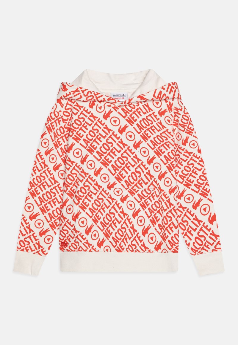 Sweat à capuche en tissu blanc présentant un motif répétitif de texte rouge avec "LACOSTE" et "NETFLIX", ainsi que des poignets et un ourlet côtelés contrastants.