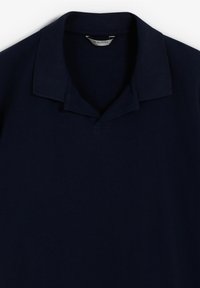 Polo de color azul marino con un cuello clásico, hecho de una tela suave. Presenta una tapeta de tres botones y sin patrones ni acentos visibles.