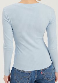 Hellblaues, geripptes Langarmshirt mit Rundhalsausschnitt, figurbetontem Design und weichem Material. Kombiniert mit hochtaillierten blauen Jeans.