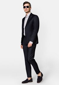 Granatowy garnitur o slim fit, z klapami w stylu notch i zapięciem na jeden guzik. Pasiasta koszula pod spodem oraz ciemne zamszowe mokasyny dopełniają całość.